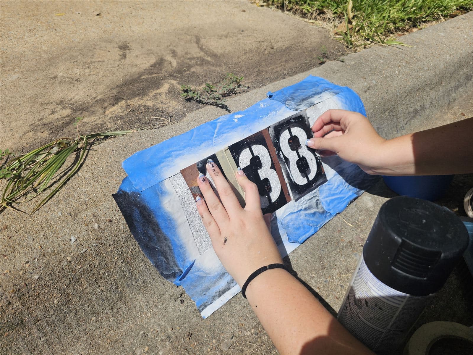 Painter aligning number stencils on a taped-off curb before spraying a fresh address