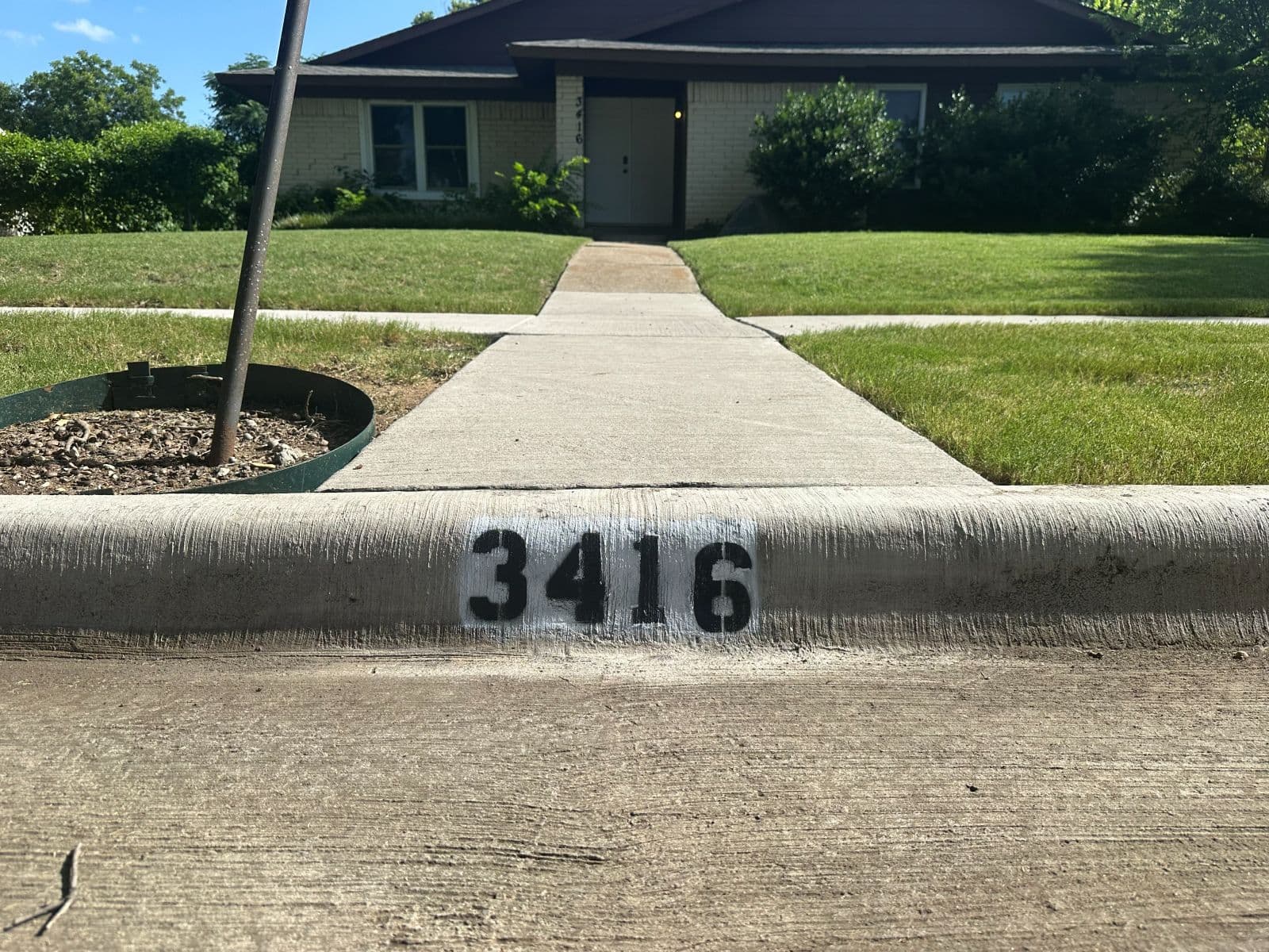 Curb address 3416 freshly painted in black on white, with the home's front walk leading to the door